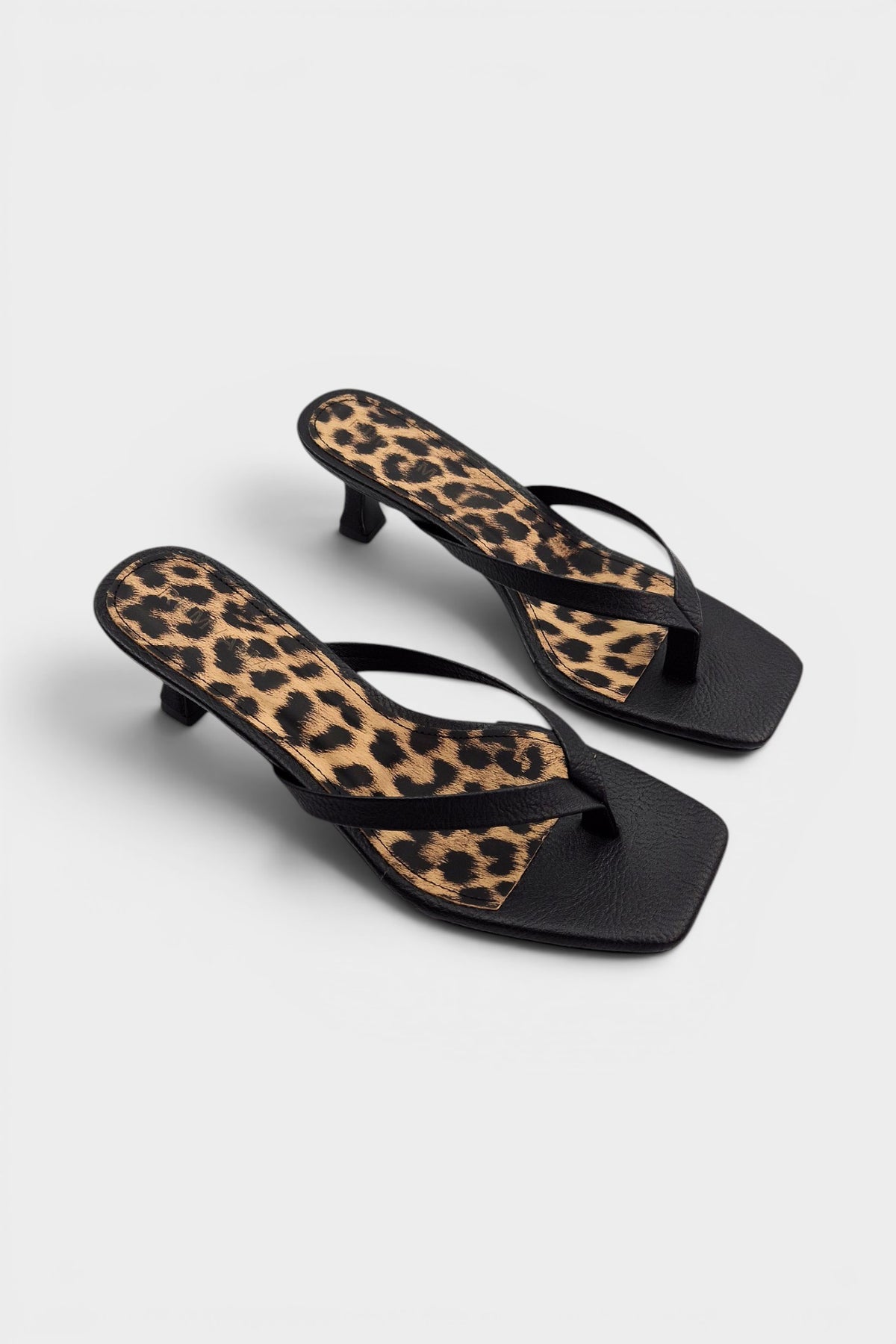 Black thong sandal mules with cheetah print insoles and kitten heels.